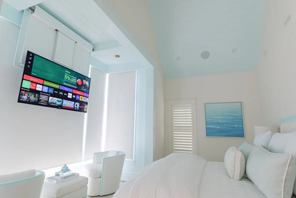 stone-harbor-primary-bedroom-drop-down-tv-deployed-cooltronics Primary bedroom of a Stone Harbor, NJ home with the ceiling-mounted drop-down TV in viewing position above the alcove, with Lutron motorized shades behind, installed by Cooltronics.