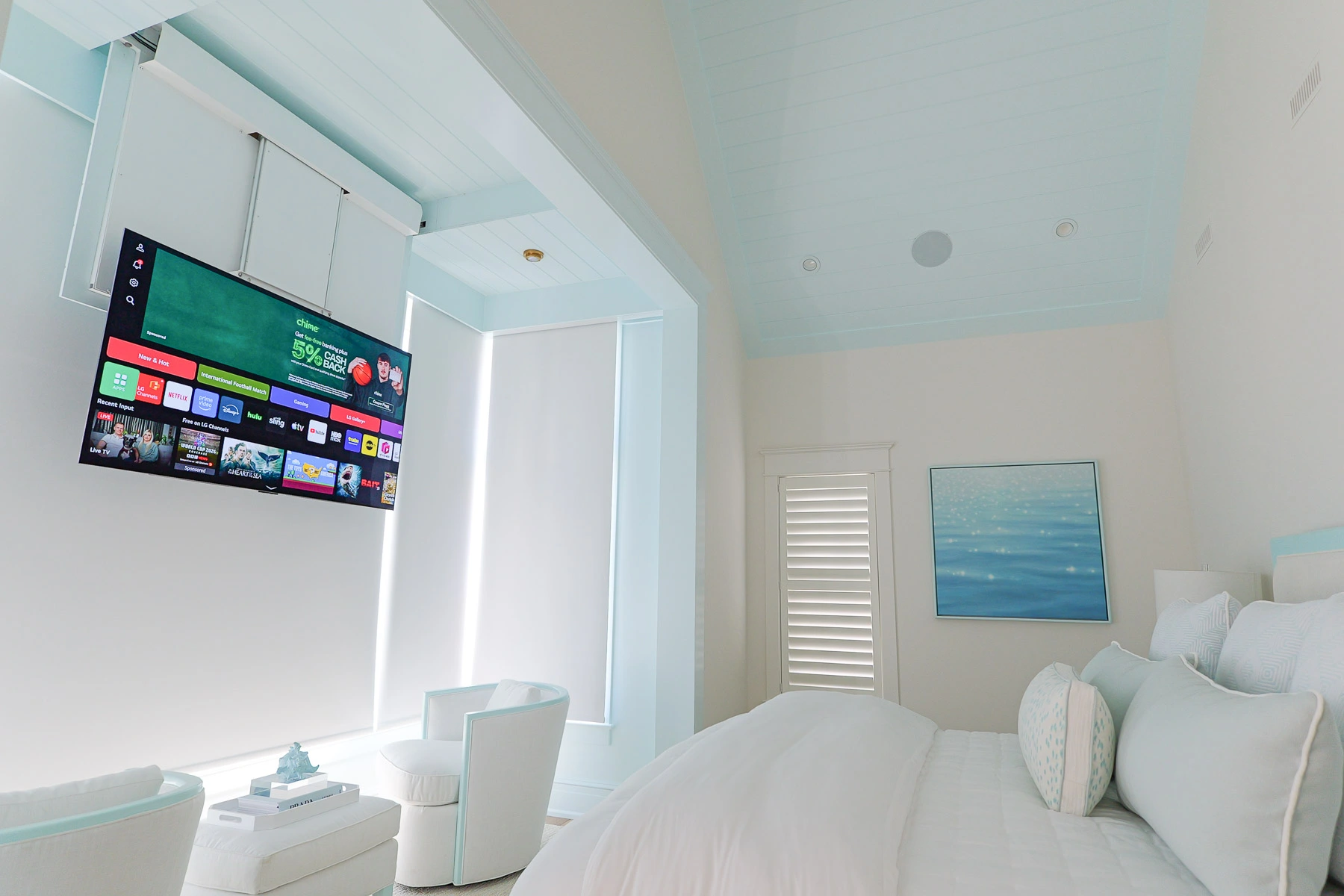 Primary bedroom of a Stone Harbor, NJ home with the ceiling-mounted drop-down TV in viewing position above the alcove, with Lutron motorized shades behind, installed by Cooltronics.