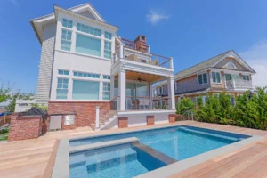 Home automation in Stone Harbor, NJ hero - Rear elevation of a Stone Harbor, NJ coastal home with pool, covered porch, and rooftop deck, integrated by Cooltronics.