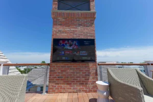 Samsung Terrace outdoor TV mounted on a brick column on the third-floor rooftop deck of a Stone Harbor, NJ home, with bay views in the background, installed by Cooltronics.
